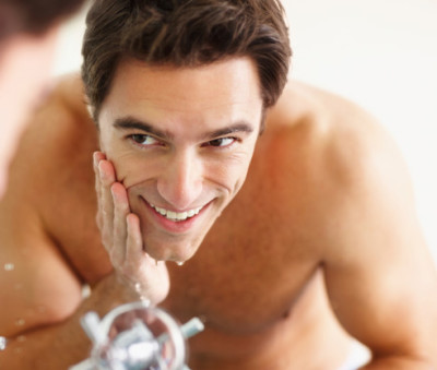 Smiling young man washing his face at the basin